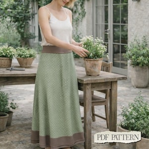May include: A high-waisted maxi skirt in sage green with a small white polka dot pattern, featuring a wide solid brown waistband and a matching solid brown hem band. The skirt is paired with a simple, sleeveless, light beige tank top.