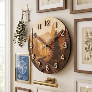 May include: A round wooden wall clock with a nature scene featuring a road winding through a forest and mountains. The clock has dark brown hands and numerals, and measures approximately 12 inches in diameter.