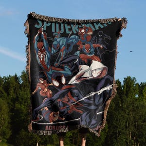 May include: Black woven throw blanket featuring multiple Spider-Man characters in various action poses. The blanket has a fringed edge and the words "SPIDER-MAN ACROSS" are visible.