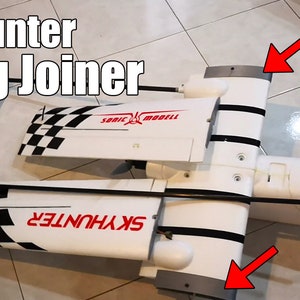 May include: A white and black chequered RC aeroplane wing with the text "SKYHUNTER" printed on the wing. The wing is attached to a white fuselage with black stripes. The image shows the wing joiner, which is a metal piece that connects the two wings.