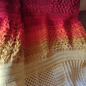 May include: A crocheted blanket with a gradient of red, orange, and yellow. The blanket is made with different crochet stitches, creating a textured and interesting design.
