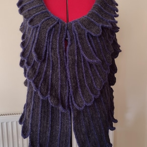 May include: A dark gray and purple knitted shawl with a scalloped edge. The shawl is draped over a dress form.