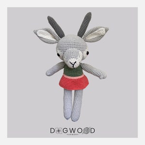 May include: A crocheted gray and white deer with green and red clothing. The deer is standing on a gray background. The text "DOGWOOD YARNER" is at the bottom of the image.