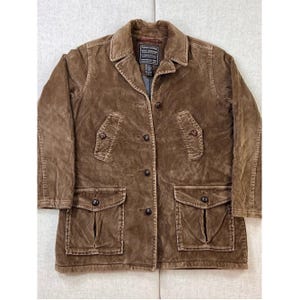 May include: A brown corduroy jacket featuring a collared neckline, a button-down front, and four front pockets with buttoned flaps. The interior label reads Abercrombie Quality Outfitters. The jacket has long sleeves and a textured fabric finish.