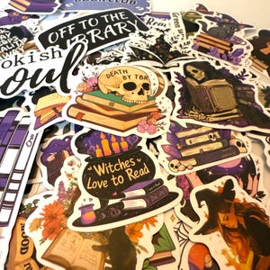 Könnte beinhalten: Eine Sammlung von Aufklebern mit einem Hexen- und Bücher-Thema. Designs umfassen Schädel auf Büchern, einen Kessel mit Kerzen und Sätze wie "Death by TBR" und "Witches Love to Read". Die Aufkleber weisen eine Vielzahl von Farben auf, darunter Lila, Schwarz und Orange.