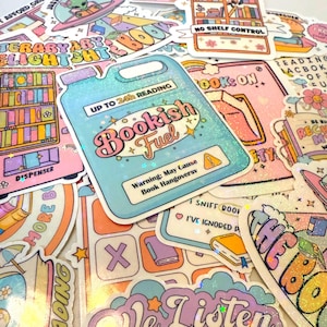 Könnte beinhalten: Eine Sammlung bunter Aufkleber zum Thema Bücher. Der zentrale Aufkleber ist ein hellblauer Kanister mit den Worten "Bookish Fuel" und "Up to 24h Reading". Weitere Aufkleber zeigen Bücher, Regenbogen und den Text "No Shelf Control".