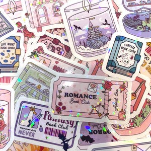 Può includere: Una collezione di adesivi colorati a tema fantasy. I disegni includono una libreria, una candela con una scena di castello e adesivi a forma di libro con testo come "Thriller Book Lover". Gli adesivi hanno una finitura olografica.