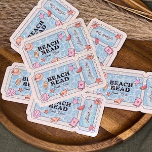 Könnte beinhalten: Eine Ansammlung hellblauer Aufkleber im Ticketdesign. Die Aufkleber zeigen den Text "BEACH READ Book Club" zusammen mit Illustrationen einer Muschel, Wassermelone, Eiscreme und eines Seesterns. Jedes Ticket hat "Admit One".