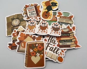 May include: A collection of fall-themed stickers featuring books, pumpkins, and autumn leaves. Some stickers have text that reads "Cozy with your Kindle", "Books are my happy", and "Her Fall". The stickers are in shades of brown, orange, and cream.