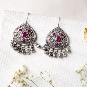 Puede incluir: Un par de pendientes de plata con un dise&ntilde;o en forma de l&aacute;grima. Los pendientes presentan un intrincado trabajo de filigrana y una piedra preciosa rosa en el centro. Los pendientes tienen un encanto colgante con peque&ntilde;as bolas de plata.