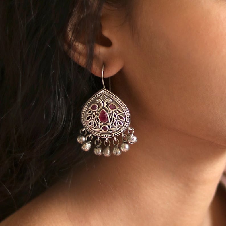 Puede incluir: Pendientes de plata con un dise&ntilde;o en forma de l&aacute;grima que presenta un motivo de pavo real y acentos de piedras preciosas rojas. Los pendientes tienen una serie de peque&ntilde;as campanas de plata que cuelgan de la parte inferior.