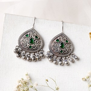 Puede incluir: Pendientes de plata con un dise&ntilde;o en forma de l&aacute;grima que presenta intrincados motivos florales y de p&aacute;jaros. Los pendientes tienen acentos de piedras preciosas verdes y cuelgan de un gancho de plata.