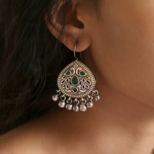 Puede incluir: Pendientes de plata con un dise&ntilde;o en forma de l&aacute;grima que presenta un motivo de pavo real y piedras verdes. Los pendientes tienen una cadena colgante de cuentas de plata.