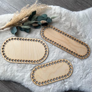 Könnte beinhalten: Drei unfertige Holz-Korbunterteile in ovaler und rechteckiger Form. Jeder Boden hat eine Reihe von gleichmäßig verteilten Löchern am Umfang. Das Holz hat eine helle, natürliche Farbe. Getrocknete Blumen und Grünzeug sind im Hintergrund.