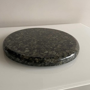 May include: A round, dark green and black granite coaster with a speckled pattern.