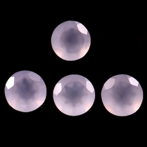 May include: Four round, faceted gemstones in a soft pink hue are displayed against a black background. The gems have a polished, reflective surface, catching the light and showcasing their cut. The arrangement is visually balanced.
