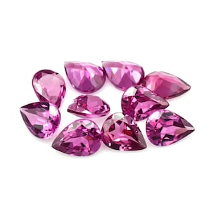 Può includere: Un gruppo di gemme sfaccettate a forma di pera, in varie tonalità di rosa e magenta, su sfondo bianco. Le sfaccettature di ogni gemma catturano la luce, evidenziando la loro forma e il colore. Ideale per la gioielleria.