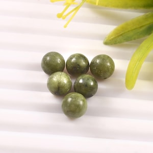 以下が含まれることがあります： 6つの丸いオリーブグリーンの宝石ビーズ。ビーズは滑らかで磨かれた表面を持ち、さまざまな緑の色合いがあります。ビーズはクラスター状に配置され、背景にはいくつかの黄色と緑の葉があります。