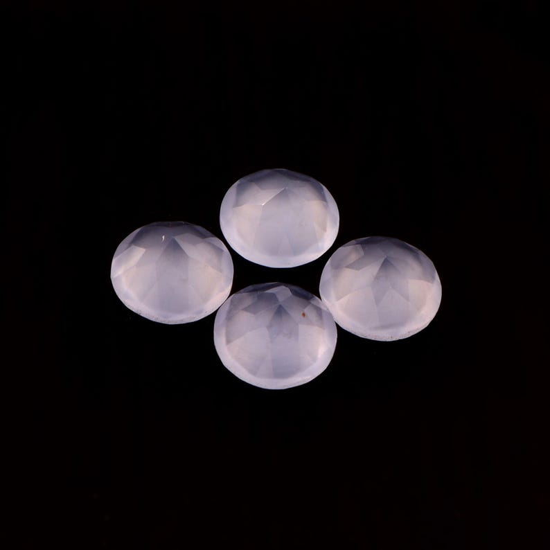May include: Four pale lavender, faceted, round gemstones are arranged against a black background. The gems have a translucent quality, with multiple facets catching the light. The overall effect is one of delicate beauty and potential for jewelry making.