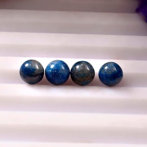 Peut inclure: Quatre pierres précieuses sphériques polies dans des tons de bleu profond et de sarcelle. Les pierres ont une surface lisse et réfléchissante, avec des variations de couleur et de texture. L'arrangement est sur une surface blanche.