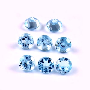 Può includere: Nove gemme rotonde, azzurre, sono disposte su uno sfondo bianco. Le gemme hanno un taglio sfaccettato, che riflette la luce e crea un effetto scintillante. Il colore è un blu chiaro e morbido, che ricorda l'acquamarina. Queste gemme potrebbero essere utilizzate per la creazione di gioielli.