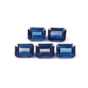 Può includere: Cinque gemme rettangolari blu scuro sono disposte su uno sfondo bianco. Ogni gemma ha una superficie lucida e riflettente e un aspetto chiaro e trasparente. Le gemme sono tagliate con bordi e angoli dritti.