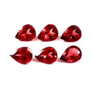 May include: Six red, teardrop-shaped gemstones are displayed against a white backdrop. Each gem is faceted, catching the light and displaying a high degree of clarity. The arrangement is symmetrical, with the gems evenly spaced, showcasing their polished surfaces.