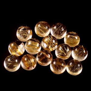 May include: A collection of clear, spherical gemstones with golden, needle-like inclusions. The spheres are arranged against a black background, showcasing the intricate patterns within each stone. These decorative spheres are ideal for collectors.