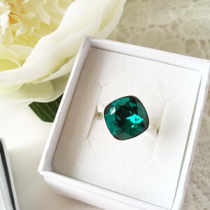 Peut inclure: Une bague avec une grande pierre précieuse vert émeraude sertie sur une bande argentée. La bague est présentée dans une boîte blanche.