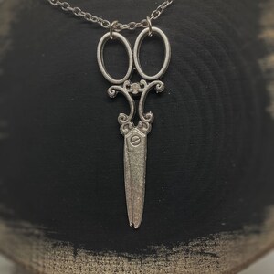 Op de afbeelding: Een zilveren ketting met een gedetailleerde schaar hanger. De ketting is delicaat en de hanger is versierd.