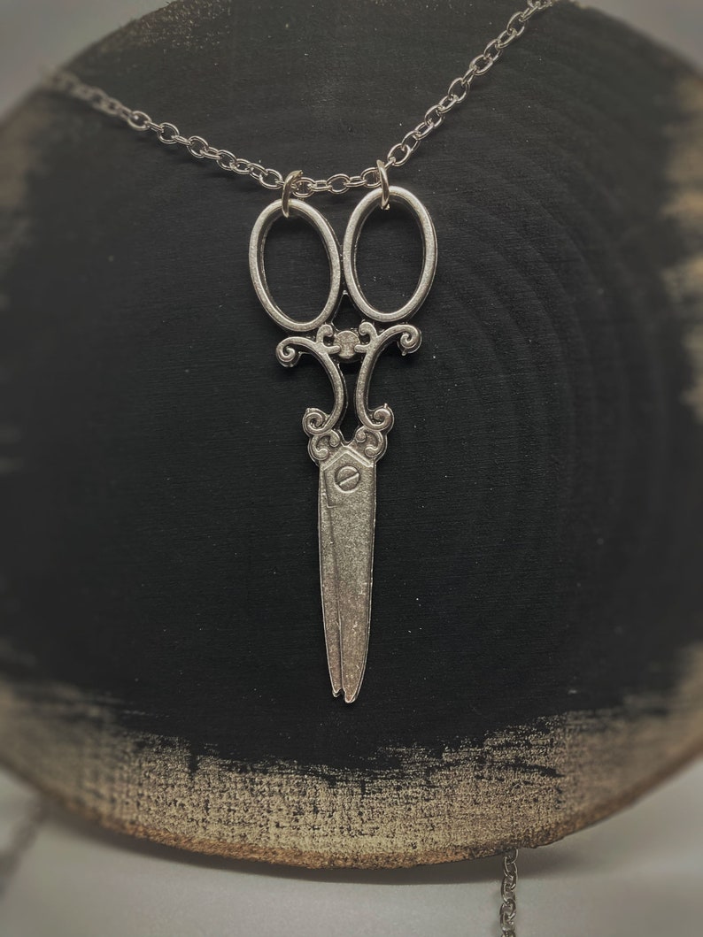 Op de afbeelding: Een zilveren ketting met een gedetailleerde schaar hanger. De ketting is delicaat en de hanger is versierd.