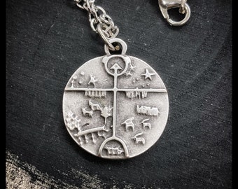 Op de afbeelding: Een zilveren ketting met een ronde hanger met een ingewikkeld ontwerp van een boom met takken en symbolen. De hanger is omgeven door een cirkel met sterren.