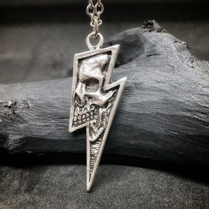 May include: Silver pendant necklace featuring a skull design inside a lightning bolt shape.