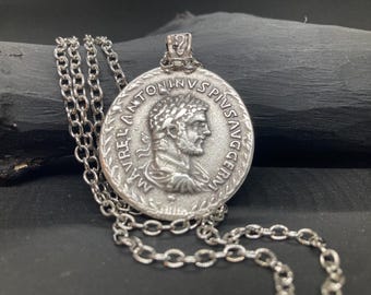 May include: A silver chain necklace with a round pendant featuring a profile of a Roman emperor. The pendant is inscribed with the text "IMP ANTONINVS PIVS AVG GERM".