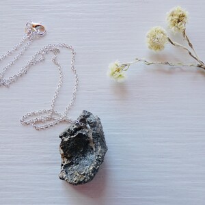May include: A silver chain necklace with a dark grey rock pendant. The rock has a rough, textured surface.