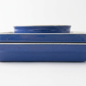 Puede incluir: Una pila de tres fuentes de horno rectangulares de cerámica con un esmalte azul intenso. Cada fuente presenta un acabado exterior liso y brillante y un borde interior blanco en contraste, con una base plana y lados ligeramente inclinados.