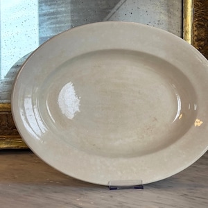 Może przedstawiać: Owalny półmisek do serwowania z gładkim, kremowobiałym szkliwionym wykończeniem. Ceramiczne naczynie posiada szeroki, płaski brzeg oraz płytki, wklęsły środek, co zapewnia czysty i neutralny wygląd odpowiedni do różnych zastosowań.