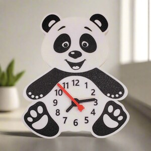 May include: A white panda bear clock with black markings. The clock face has black numbers and red hands. The panda has a black nose and black eyes.
