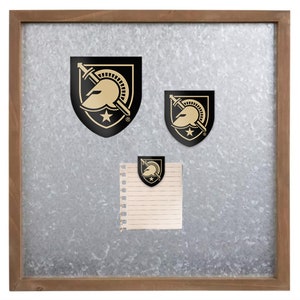 May include: A metal bulletin board with a wood frame. Three gold and black stickers of a Spartan helmet with a sword are attached to the board. A small notepad with lined paper is attached to the board with a gold and black sticker.
