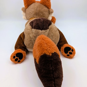 Puede incluir: Un peluche de zorro, visto desde atr&aacute;s, con tonos marrones y naranjas. El zorro tiene grandes orejas esponjosas, una larga cola y almohadillas negras. El juguete es suave y tierno, perfecto para ni&ntilde;os.