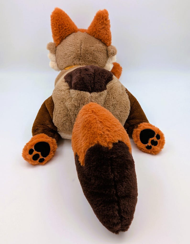 Puede incluir: Un peluche de zorro, visto desde atr&aacute;s, con tonos marrones y naranjas. El zorro tiene grandes orejas esponjosas, una larga cola y almohadillas negras. El juguete es suave y tierno, perfecto para ni&ntilde;os.