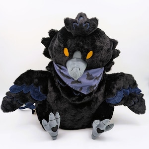 May include: A plush black bird with a blue bandana and wings. The bird has yellow eyes and gray feet with heart-shaped details. The wings have blue accents. The bird is a backpack.