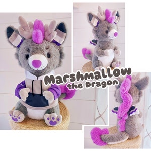 May include: A gray plush dragon with purple accents and a pink mohawk. The dragon is wearing a gray hoodie with a black zipper and purple sleeves. The dragon is sitting on a woven basket. The text "Marshmallow the Dragon" is written in a purple font on a white background.