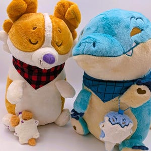 May include: Two plush toys: a corgi-like dog with orange and white fur, wearing a red and black plaid bandana, and a blue alligator-like creature with a blue bandana. A small plush dog is in front of the corgi.