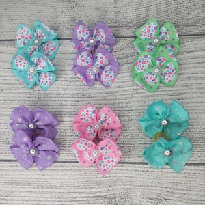 May include: Six sets of colorful hair bows. Each bow is made of ribbon and features a polka dot pattern in various colors, including teal, purple, pink, and green. A pearl bead is in the center of each bow.