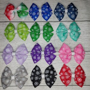May include: Twelve pairs of snowflake patterned hair bows in various colors, including red, green, blue, purple, pink, gray, and black. The bows are arranged in four rows of three.