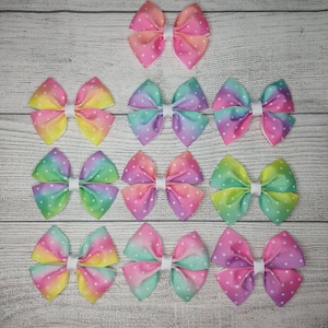 May include: Twelve pastel ombre hair bows with white polka dots. The bows are arranged in three rows of four. The bows are made of ribbon and have a white center.