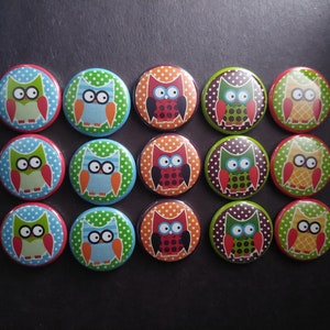 May include: A set of 15 colorful owl buttons with different patterns and colors. The buttons are round and have a white background with black polka dots. The owls are all different colors and have different expressions.