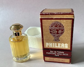 May include: A small bottle of Phileas Eau de Toilette by Parfums Nina Ricci. The bottle is clear glass with a gold cap and a gold label. The box is red and gold with a picture of a hot air balloon.