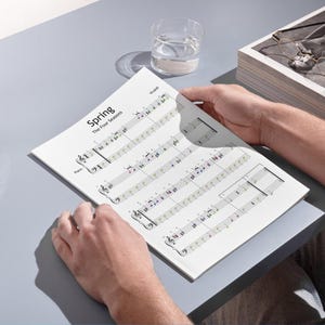 May include: A sheet music page from Vivaldi's "The Four Seasons" featuring the title "Spring". The music is for piano, with colorful notes. A glass of water and a box are in the background.